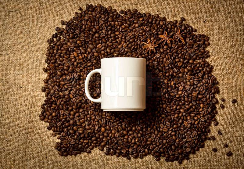 Big white mug lying on pile of roasted coffee beans on linen cloth, stock photo