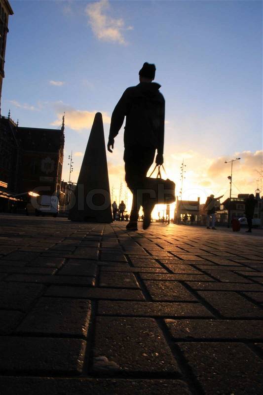The man with cap and handbag walks to the Central Station in Amsterdam by sunrise, stock photo