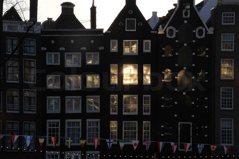 Facade of houses and a line of flags from countries of the world in Amsterdam by sunrise, stock photo