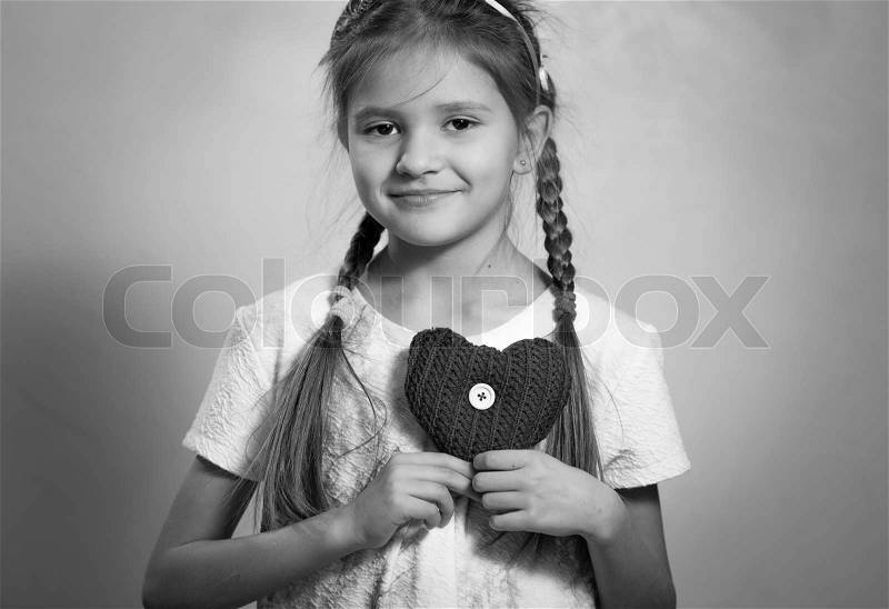 Monochrome portrait of cute smiling girl holding decorative heart on chest, stock photo