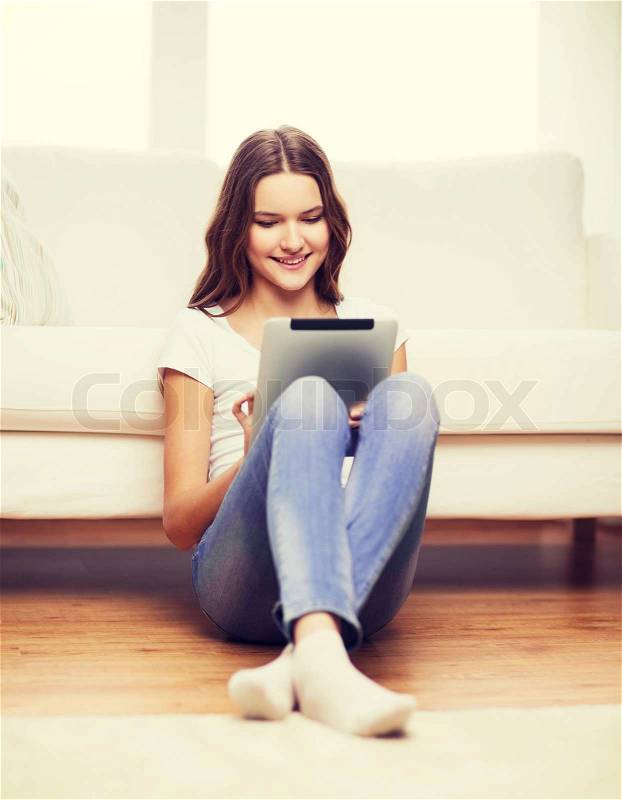 Home, technology and internet concept - smiling teenage girl sitting ong the floor with tablet pc computer at home, stock photo