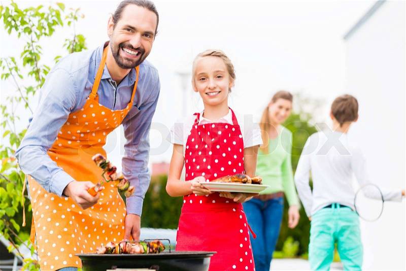 Father and daughter barbecue meat spits and sausages at family garden BBQ , stock photo