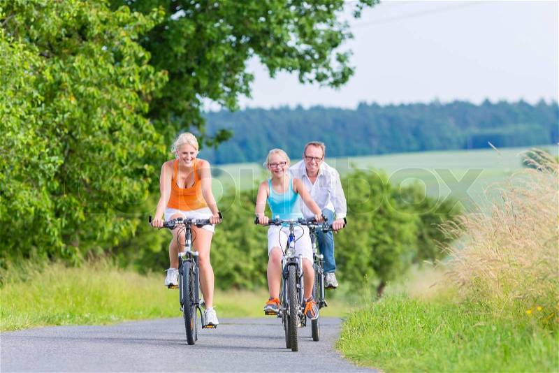 Parents and daughter have bicycle or bike tour on country lane, stock photo