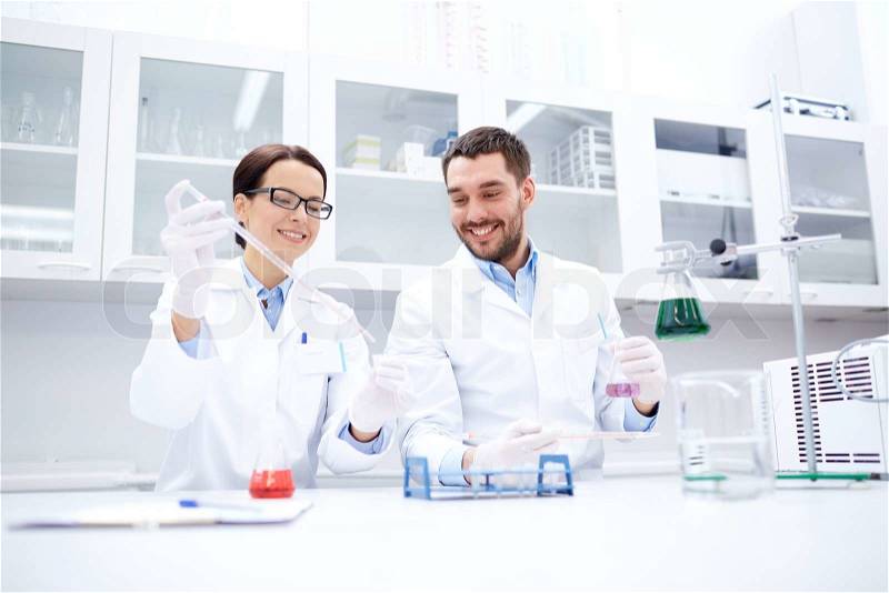 Science, chemistry, technology, biology and people concept - young scientists with pipette and glass making test or research in clinical laboratory, stock photo