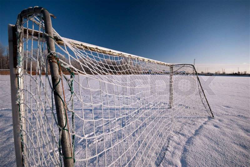 Soccer goal with icy net and soccer field in winter snow all over, stock photo