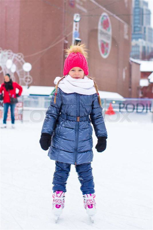 Adorable little girl skating on the ice rink outdoors, stock photo