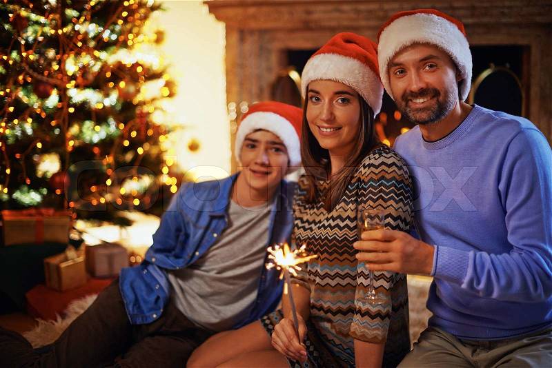 Happy couple in Santa caps toasting with their son on background, stock photo