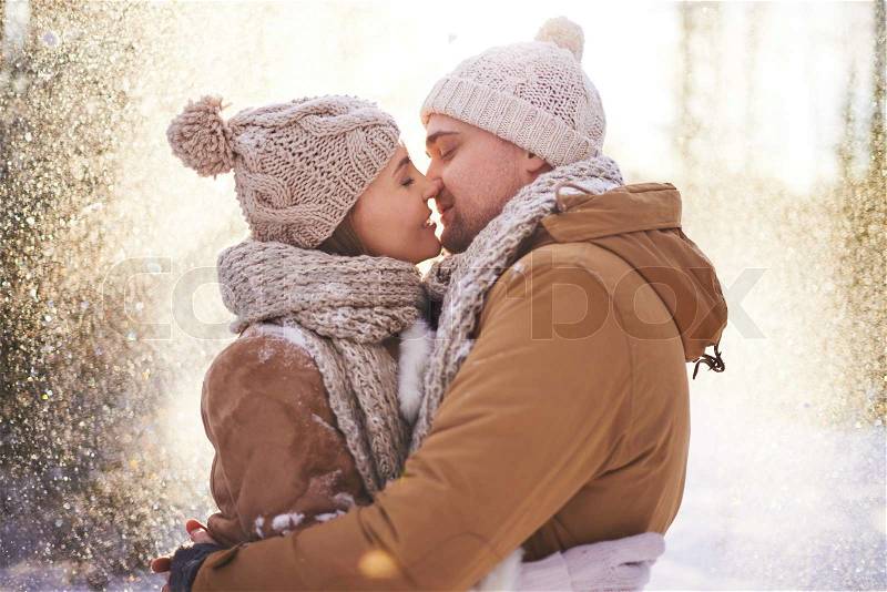 Happy young man and woman kissing in snowfall, stock photo
