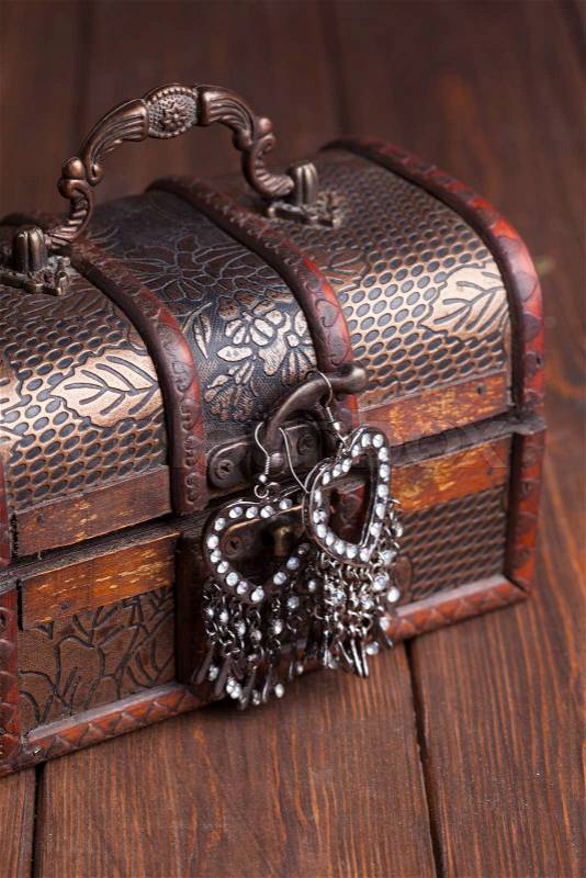 Vintage earrings in a form of hearts hanging on old treasure chest, stock photo