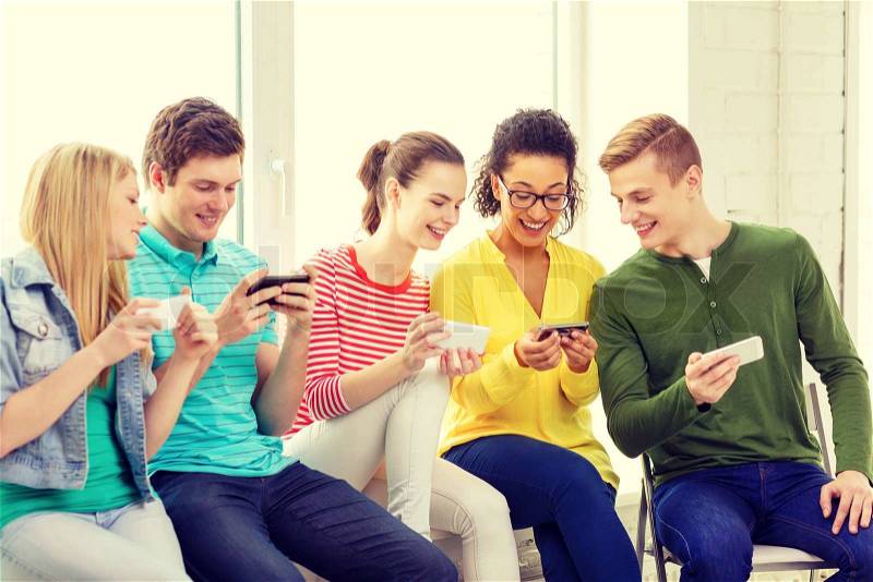 Education, school and technology concept - smiling students with smartphone texting at school, stock photo