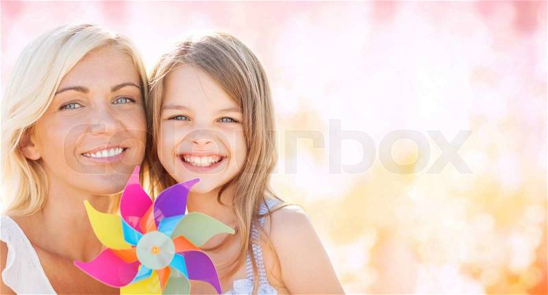 Summer holidays, family, children and people concept - happy mother and girl with pinwheel toy over pink lights background, stock photo