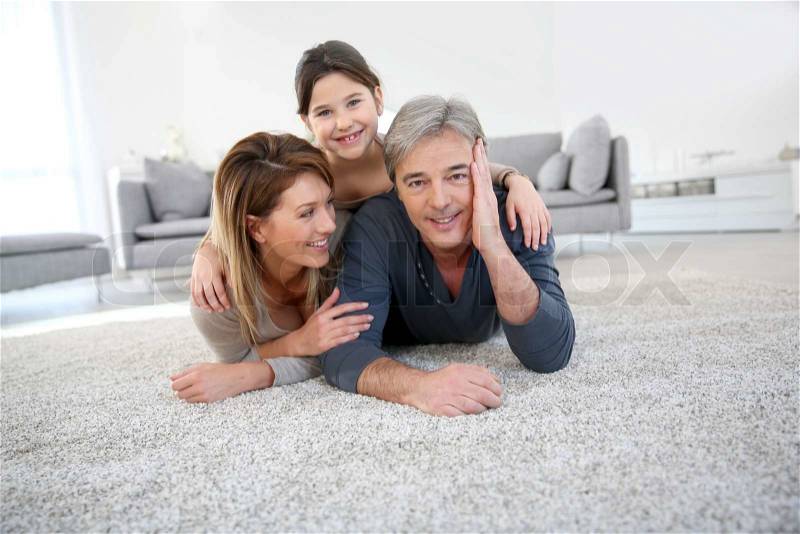 Middle-aged couple with little girl laying on carpet, stock photo