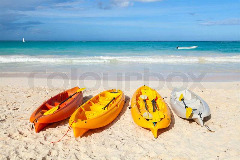 Colorful plastic kayaks lay on empty sandy beach. Coast of Atlantic ocean, Dominican republic, stock photo