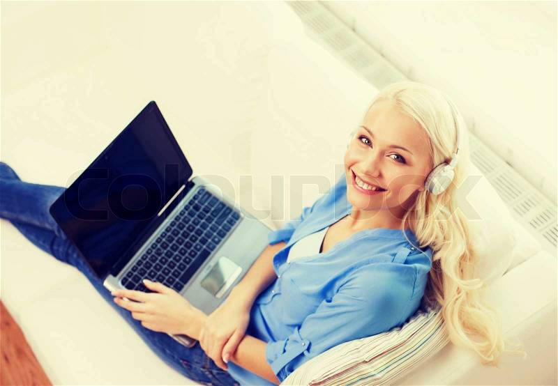 Home, music, technology and internet concept - smiling woman lying on the couch with laptop computer and headphones at home, stock photo