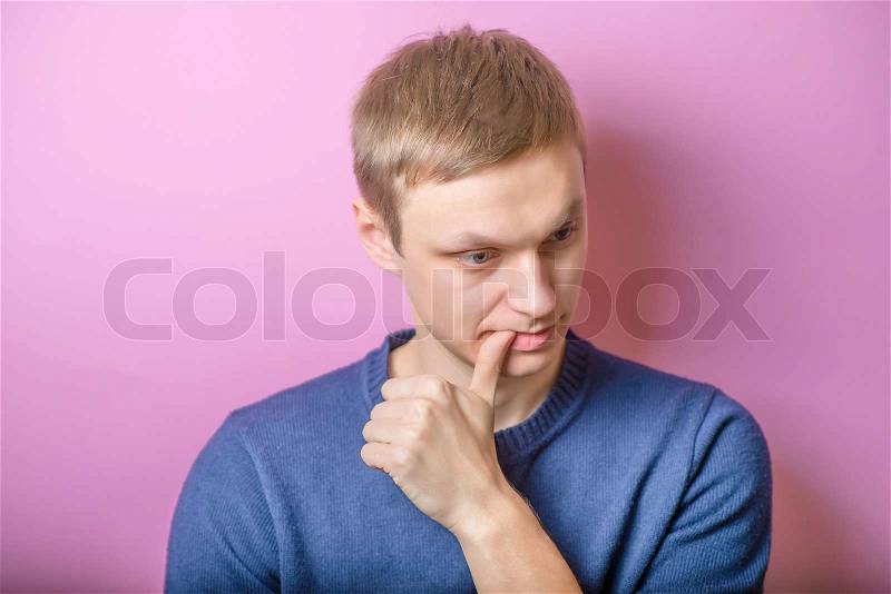 Sad young man looking down, finger to his mouth. Gesture. On a purple background, stock photo