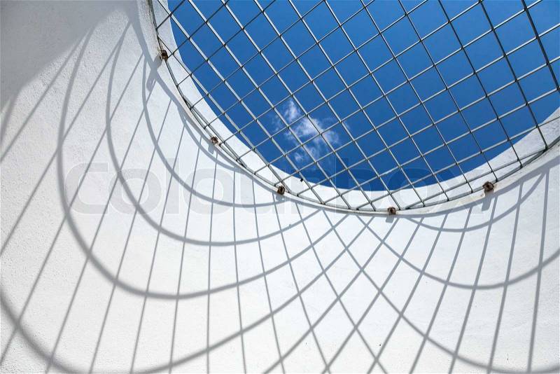 Abstract white interior fragment. Blue sky behind the round window with metal grid, stock photo