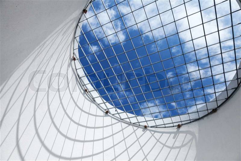 Abstract white interior fragment. Blue cloudy sky behind the round window with metal grid, stock photo