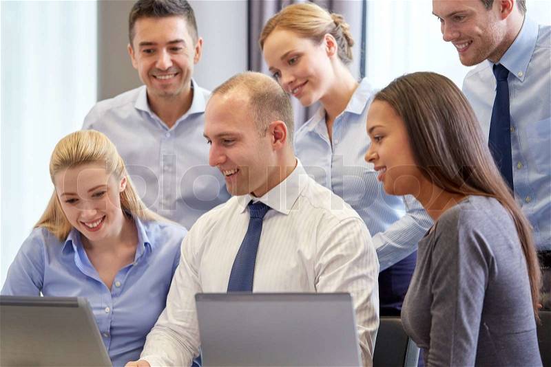 Business, people and technology concept - smiling business team with laptop computer meeting in office, stock photo