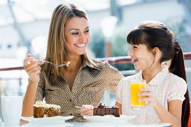 Mother and daughter having cake and juice at cafe, stock photo