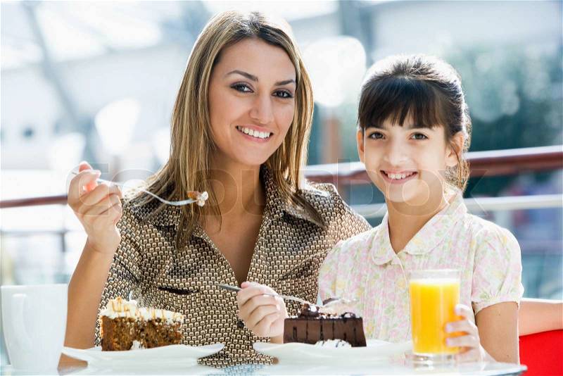 Mother and daughter eating cake in cafe together, stock photo