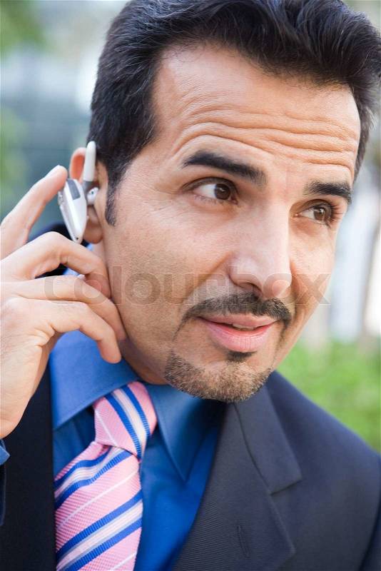 Businessman using bluetooth earpiece outside, stock photo
