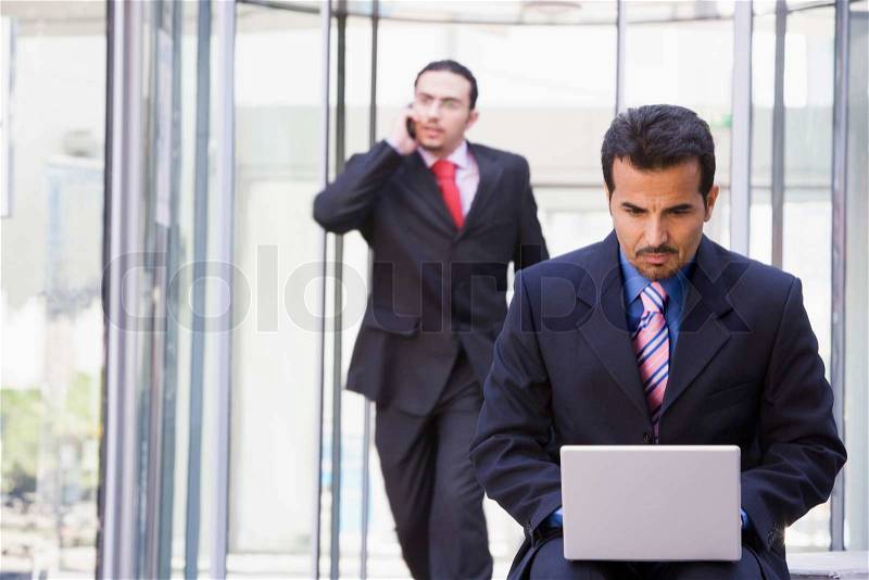 Businessman working at laptop outside office, stock photo