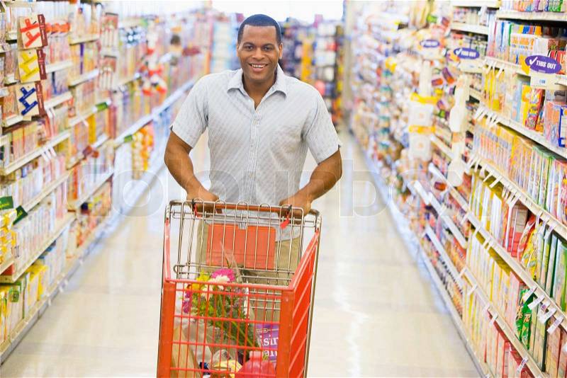 Man pushing trolley along supermarket grocery aisle, stock photo