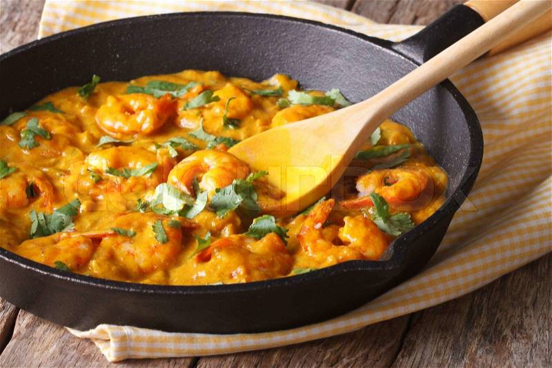 Prawns in curry sauce in a black frying pan close-up. Horizontal , stock photo