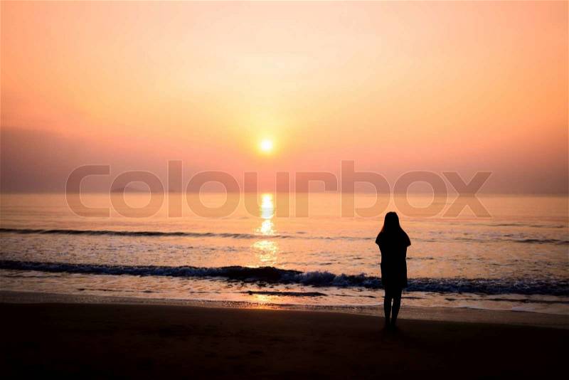 Silhouette of woman alone and wave on the beach with sunset in the sea, stock photo