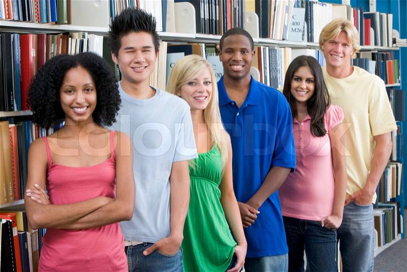 Group of six students standing in front of library bookshelves, stock photo