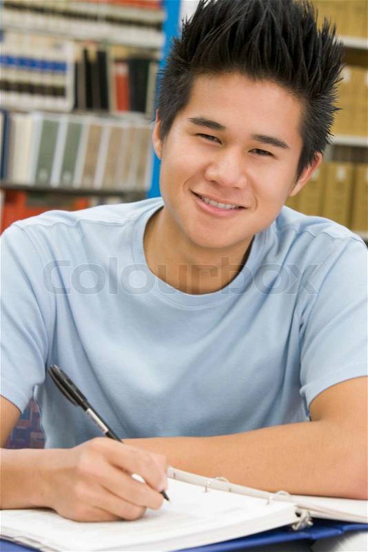 Male university student writing report in library, stock photo