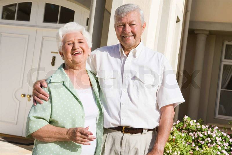 Senior couple standing outside front door of home, stock photo