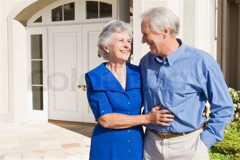 Senior couple standing outside front door of house, stock photo