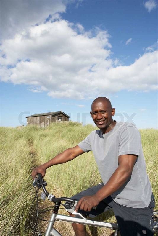 Young Man Riding Mountain Bike By Dunes With Old Beach Hut In Distance, stock photo