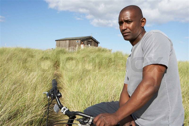 Young Man Riding Mountain Bike By Dunes With Old Beach Hut In Distance, stock photo