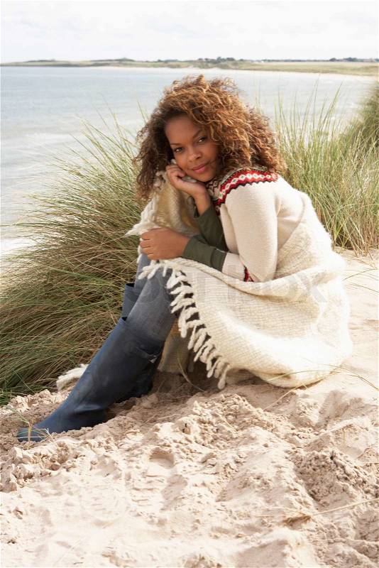 Young Woman Sitting In Sand Dunes Wrapped In Blanket, stock photo