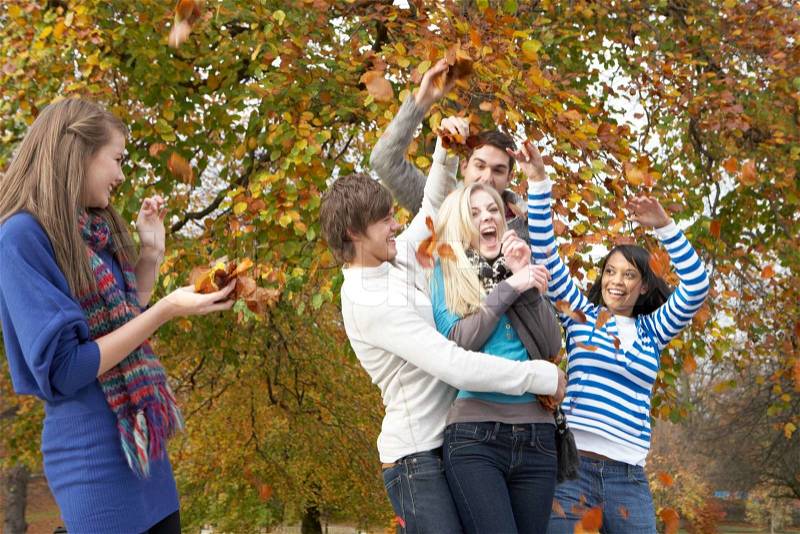 Group Of Teenage Friends Throwing Leaves In Autumn Landscape, stock photo