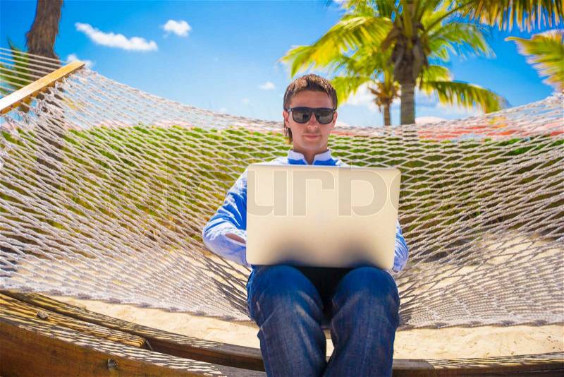 Young man working with laptop in hammock during beach vacation, stock photo