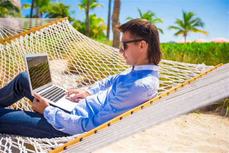 Young man working with laptop in hammock during beach vacation, stock photo