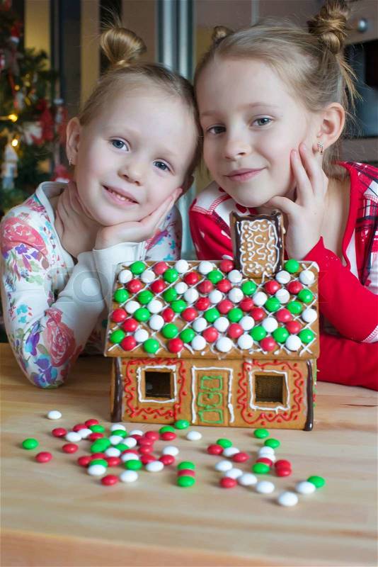 Little adorable girls decorating gingerbread house for Christmas, stock photo