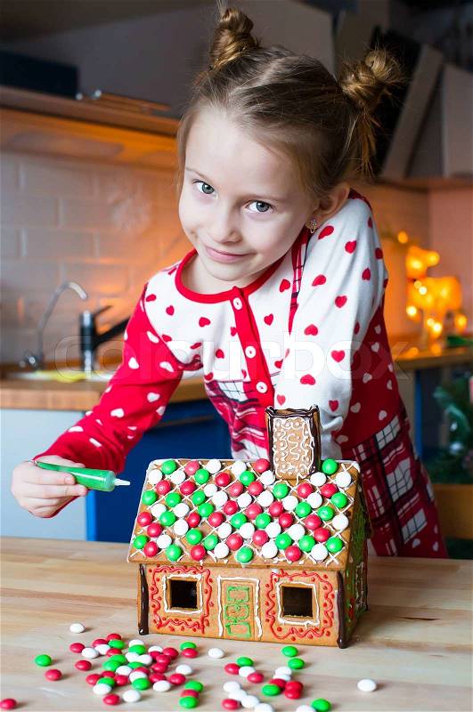 Little adorable girl decorating gingerbread house for Christmas, stock photo