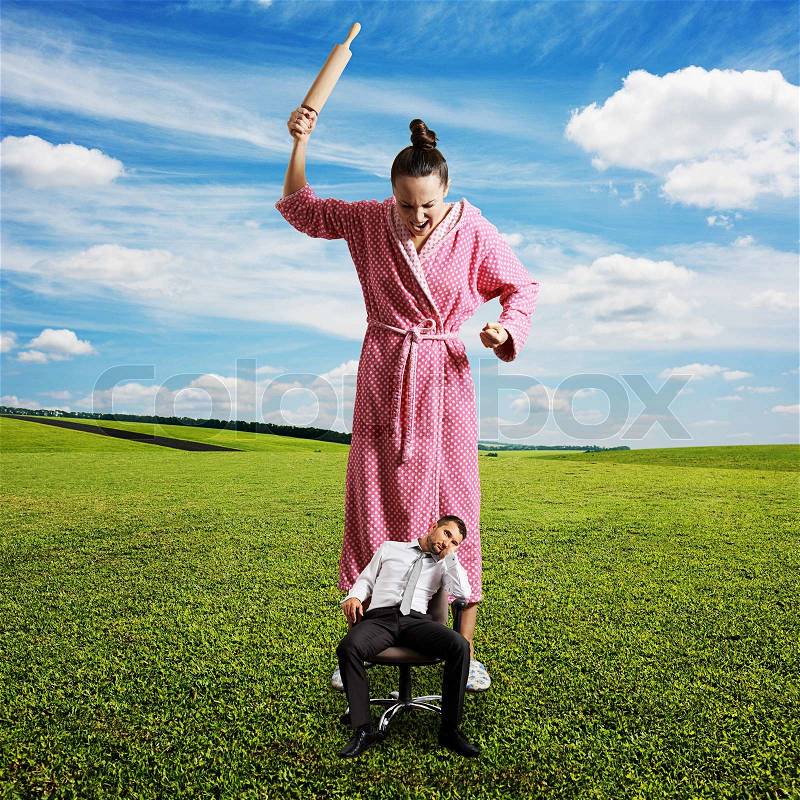 Dissatisfied woman with rolling pin screaming at small lazy man on the chair. photo at outdoor, stock photo