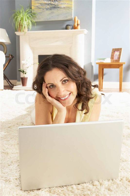 Woman Using Laptop Relaxing Laying On Rug At Home, stock photo