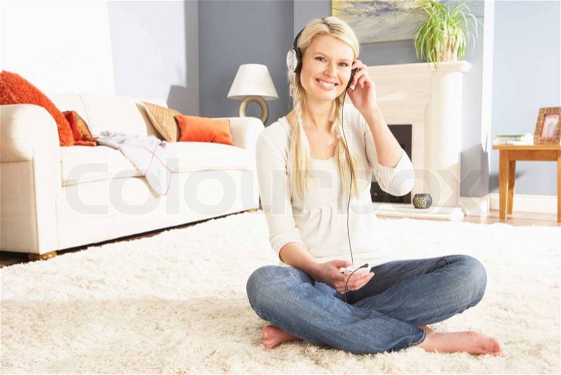 Woman Listening To MP3 Player On Headphones Relaxing Sitting On Rug At Home, stock photo