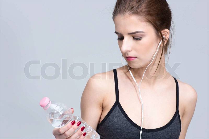 Portrait of a sporty woman in headphones looking on the bottle with water, stock photo