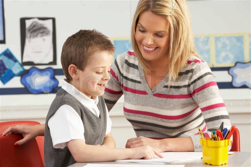 Male Primary School Pupil And Teacher Working At Desk In Classroom, stock photo
