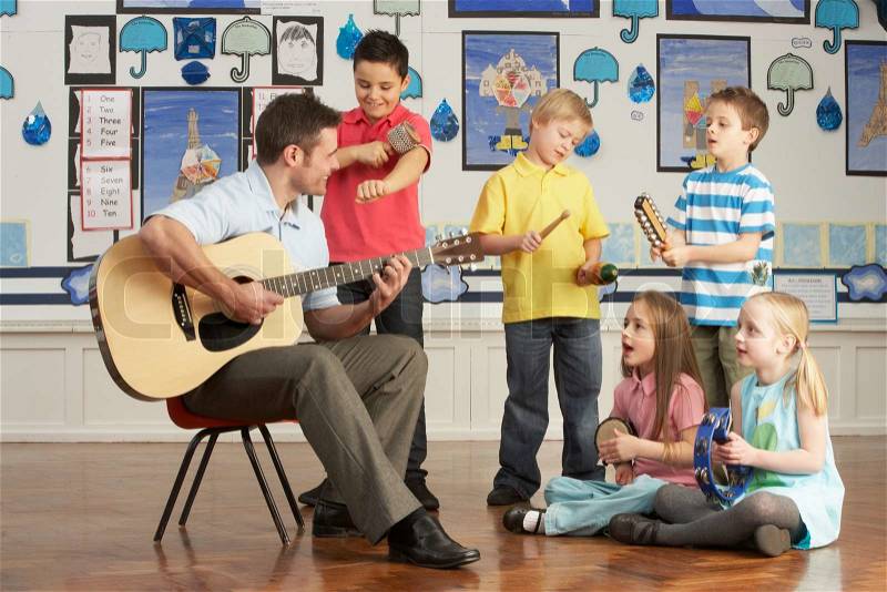 Male Teacher Playing Guitar With Pupils Having Music Lesson In Classroom, stock photo