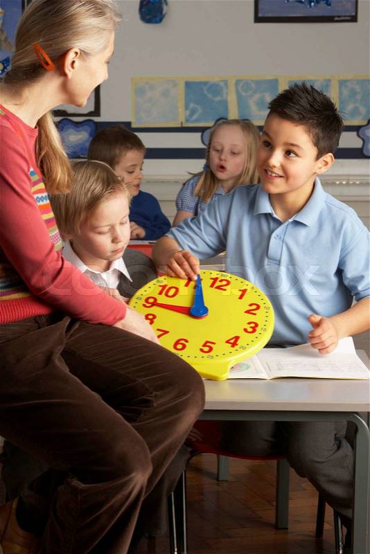 Female Teacher In Primary School Teaching Children To Tell Time In Classroom, stock photo