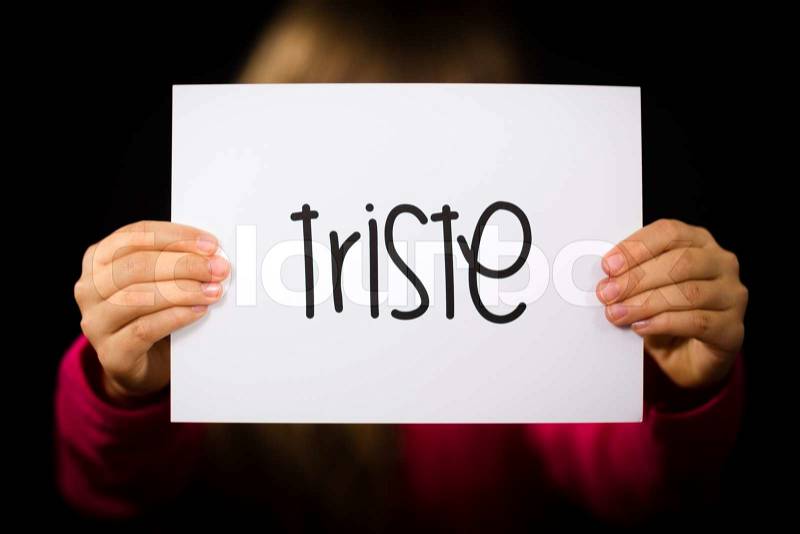 Studio shot of child holding a sign with Spanish word Triste - Sorry, stock photo