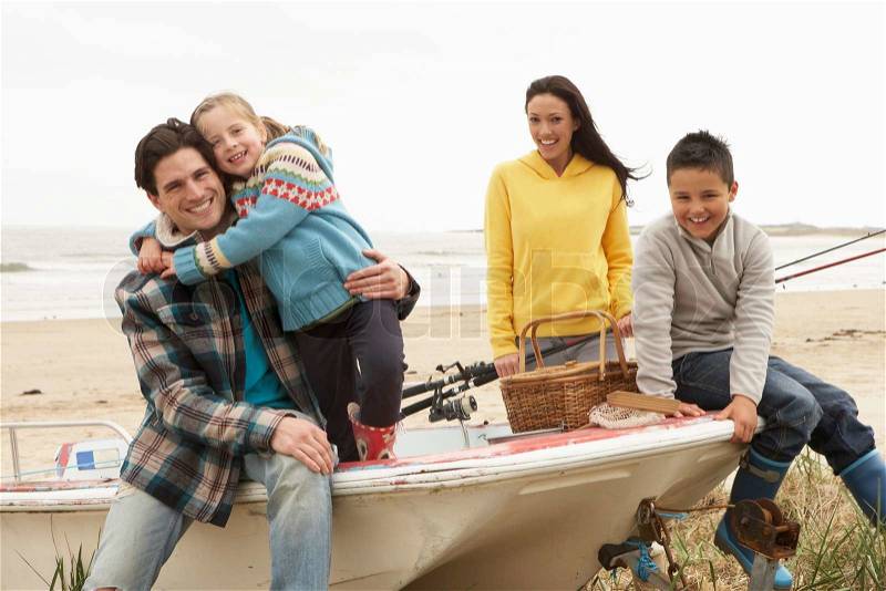 Family Group Sitting On Boat With Fishing Rod On Winter Beach, stock photo